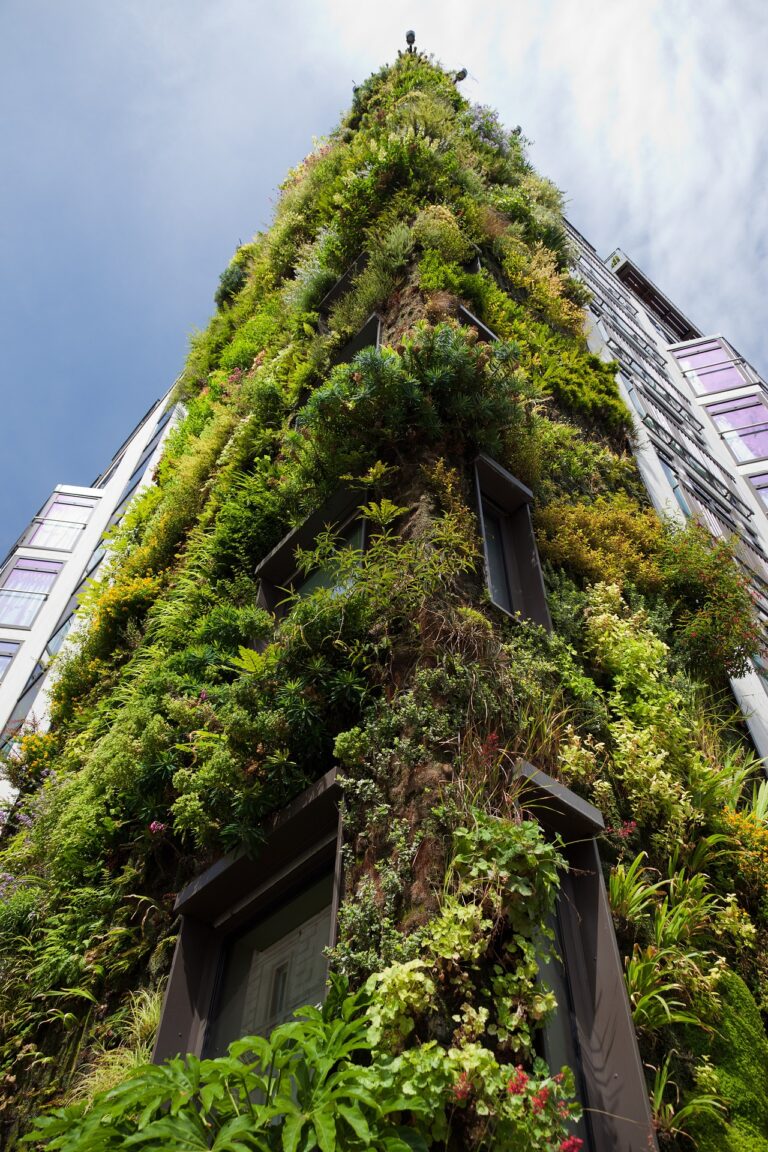 Edificio alto, en plano contrapicado, con la fachada llena de plantas en las que predomina el color verde.