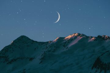 Una montaña nevada bajo el cielo nocturno estrellado con una luna creciente.