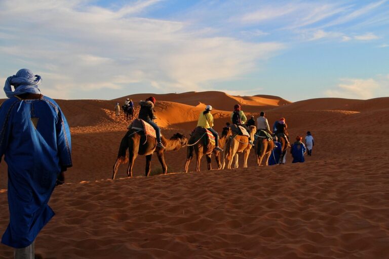Caravana de personas que viajan a pie y a camello por el desierto.
